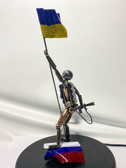 Soldado ucraniano con bandera, de pie sobre el harapo rasgado de un orco (27cm)