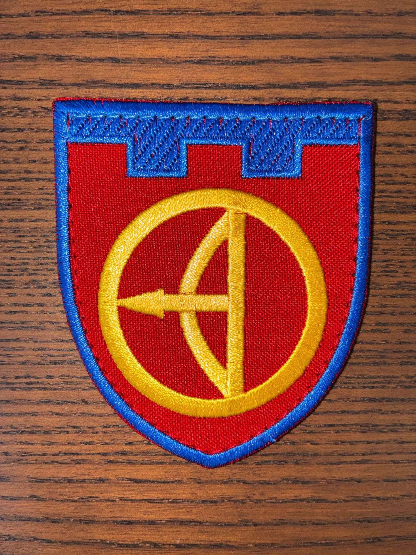 Patch - 112th Territorial Defense Brigade in red and blue embroidered fabric, featuring a yellow circular emblem and arrow
