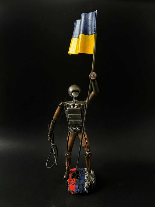 Ukrainian soldier sculpture with flag standing on Russian rag made from frontline shells
