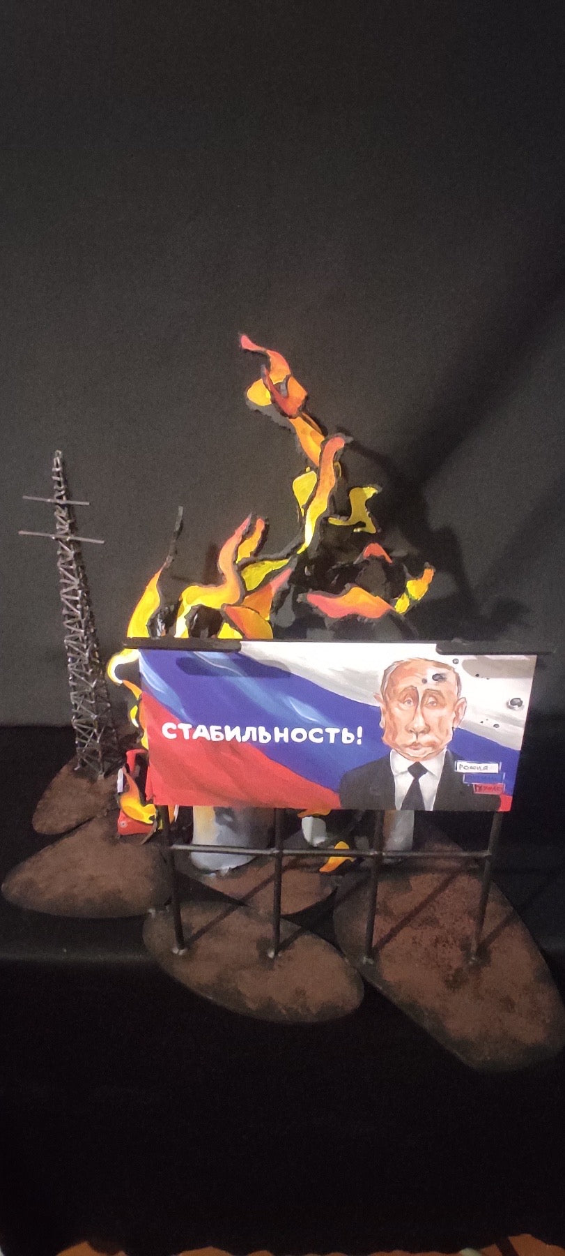 Billboard promoting 'Stability' next to burning oil storage containers in artwork inspired by Russian billboards