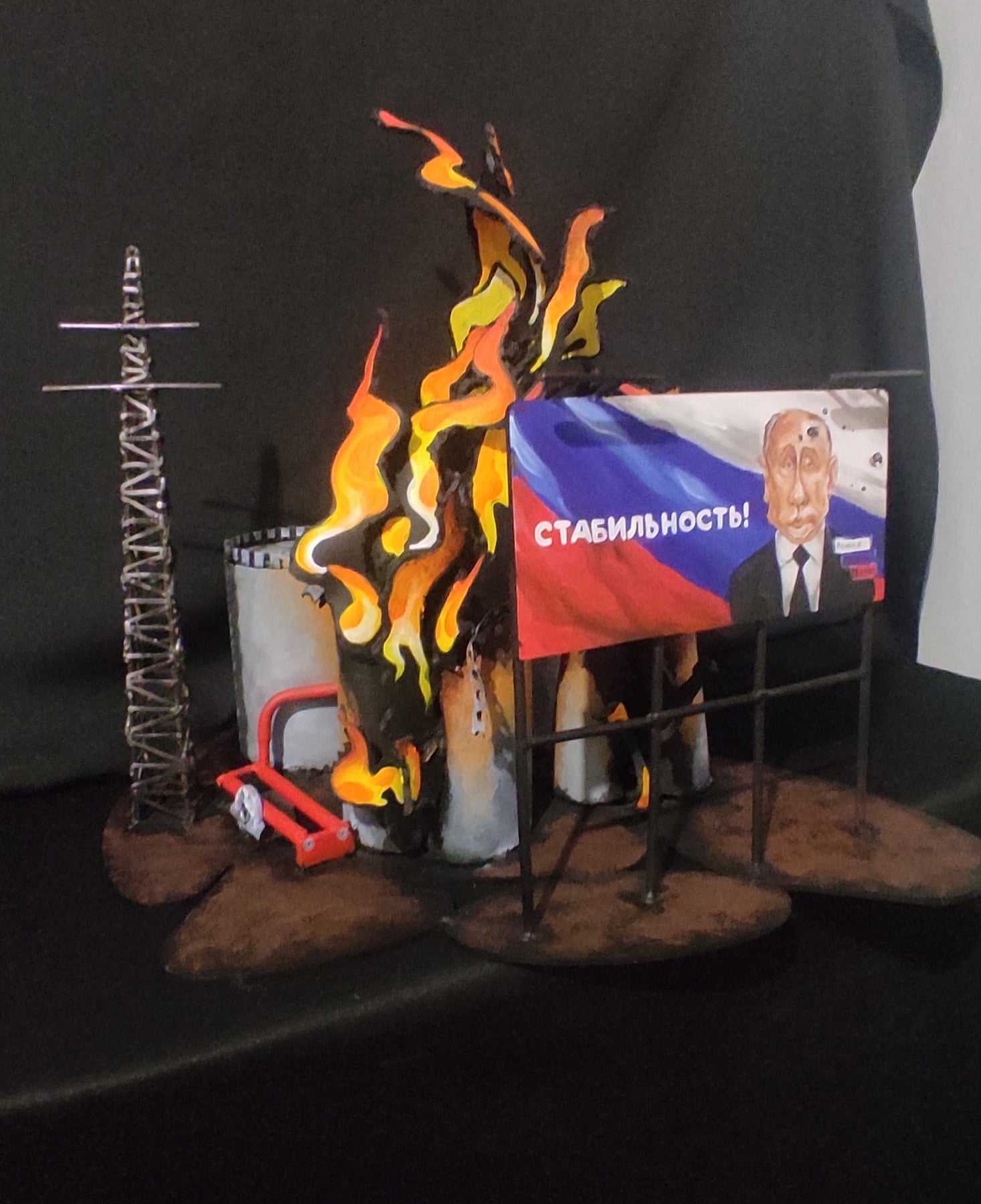 Billboard promoting Stability next to burning oil storage containers in artwork inspired by Russia's billboards
