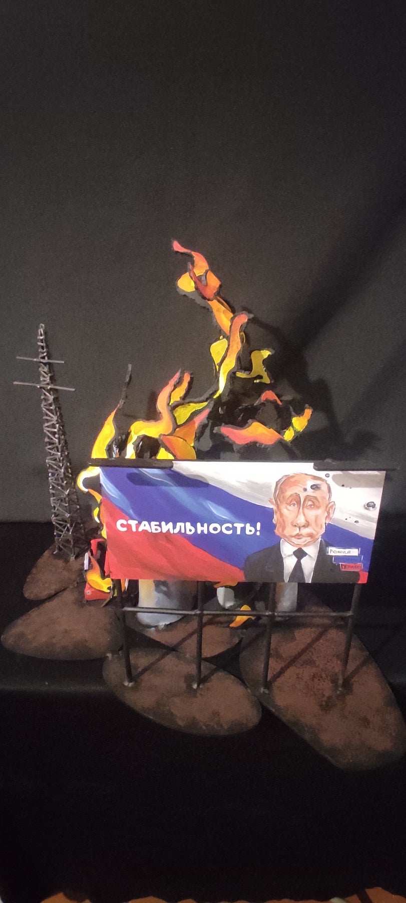 Billboard promoting 'Stability' next to burning oil storage containers in artwork inspired by Russian billboards