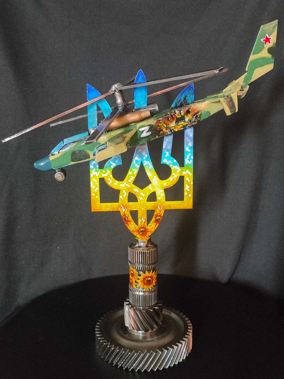 Destroyed KA-52 attack helicopter model impaled on Tryzub sculpture by Hisoshi Art Studio