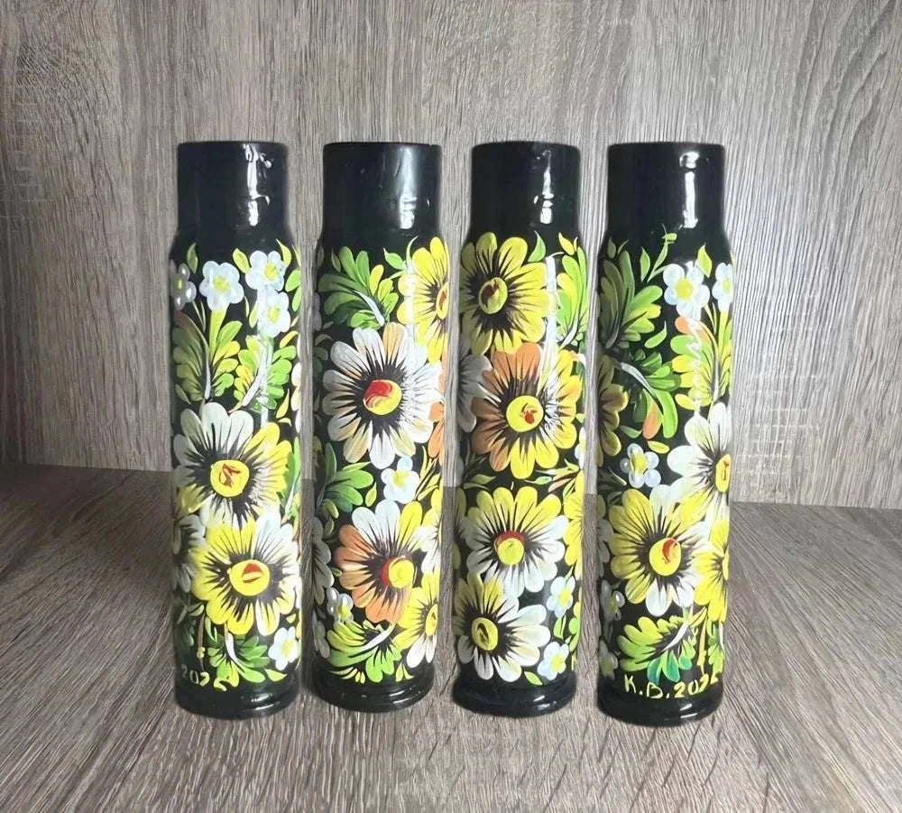 Ukrainian reward system: four black shell casings hand-painted with bright yellow and white flowers and green leaves