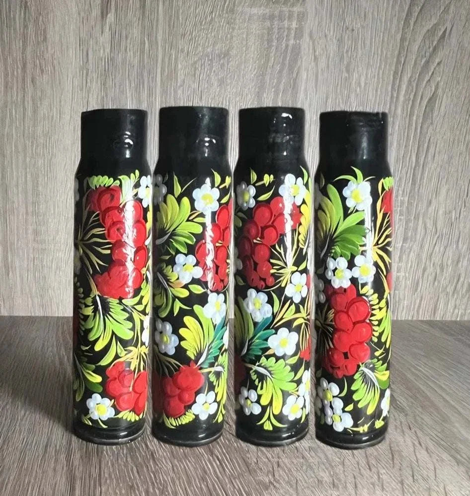 Ukrainian reward system displayed as four black painted shell casings with vivid red flowers, white blossoms and green leaves