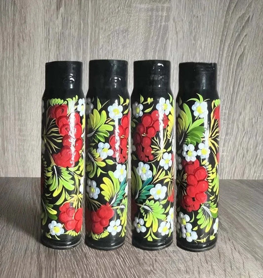 Ukrainian reward system displayed as four black painted shell casings with vivid red flowers, white blossoms and green leaves