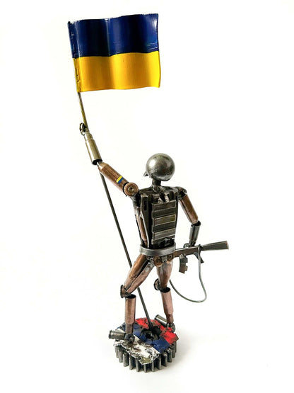 Ukrainian soldier sculpture with flag standing on Russian rag made from frontline shells