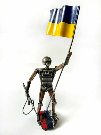 Sculpture of a Ukrainian soldier holding a flag standing on a Russian rag made from frontline shells