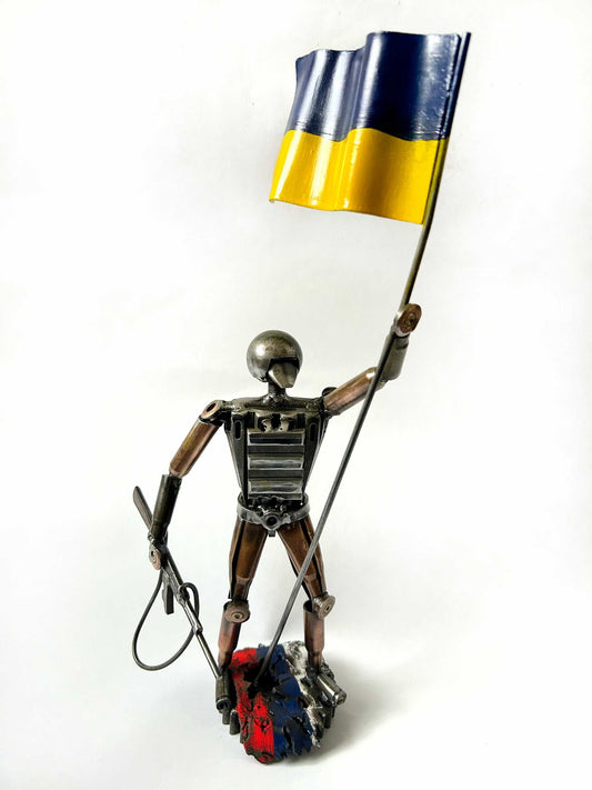 Sculpture of a Ukrainian soldier holding a flag standing on a Russian rag made from frontline shells
