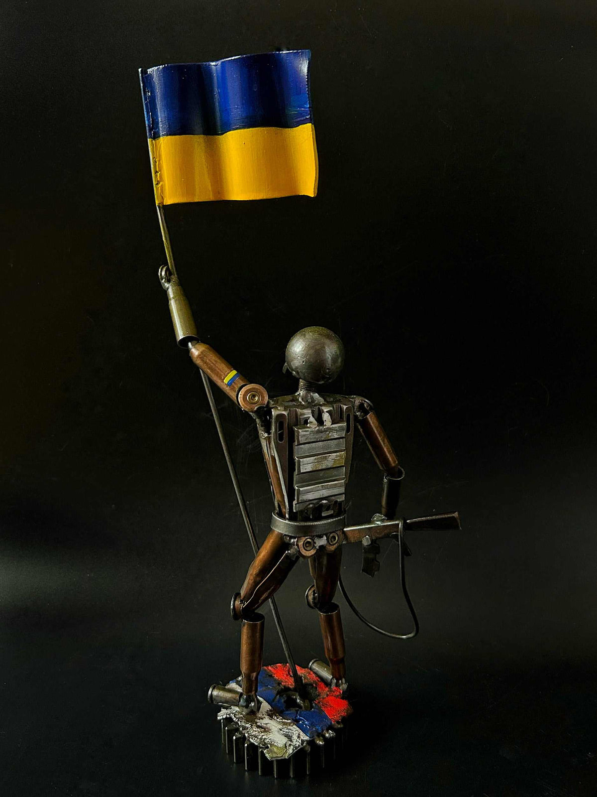 Ukrainian soldier sculpture with flag standing on Russian rag made from frontline shells